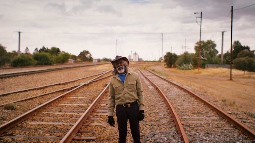 Actor David Gulpilil, an older Yolngu man standing on empty train tracks, in the documentary My Name is Gulpilil