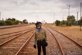 Actor David Gulpilil, an older Yolngu man standing on empty train tracks, in the documentary My Name is Gulpilil