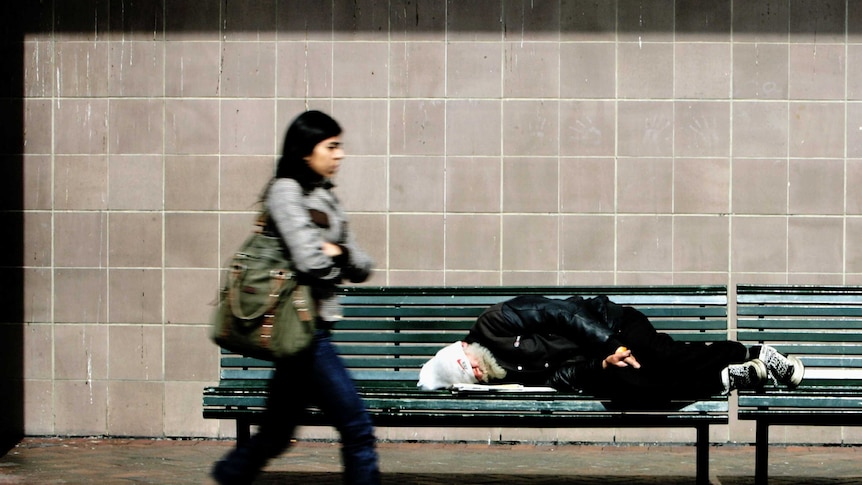 Homeless man sleeping on a bench in Sydney.