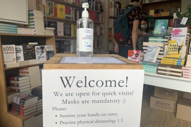 A bottle of hand sanitiser sits on a box with a welcome sign inside a bookshop.