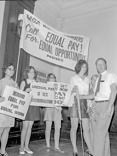 A woman holds a banner with several other young women at an equal pay protest at Melbourne Town Hall.