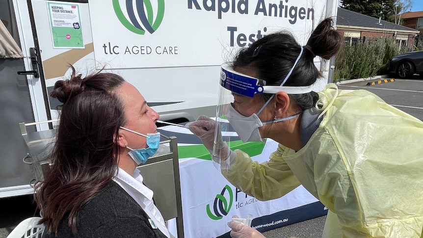 A staff member in COVID-19 protective gear putting a nasal swap in a visitors nose.