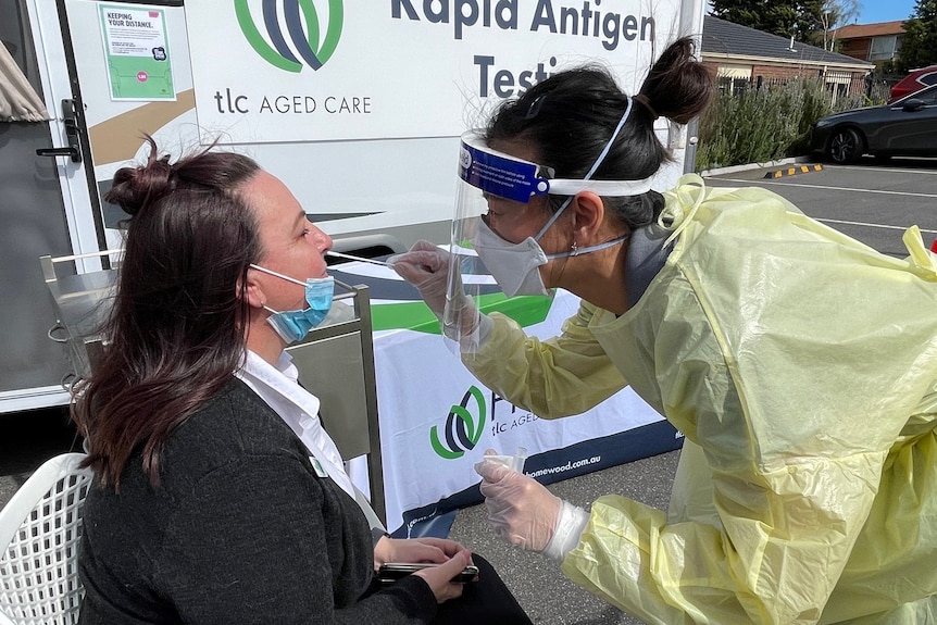 A staff member in COVID-19 protective gear putting a nasal swap in a visitors nose.