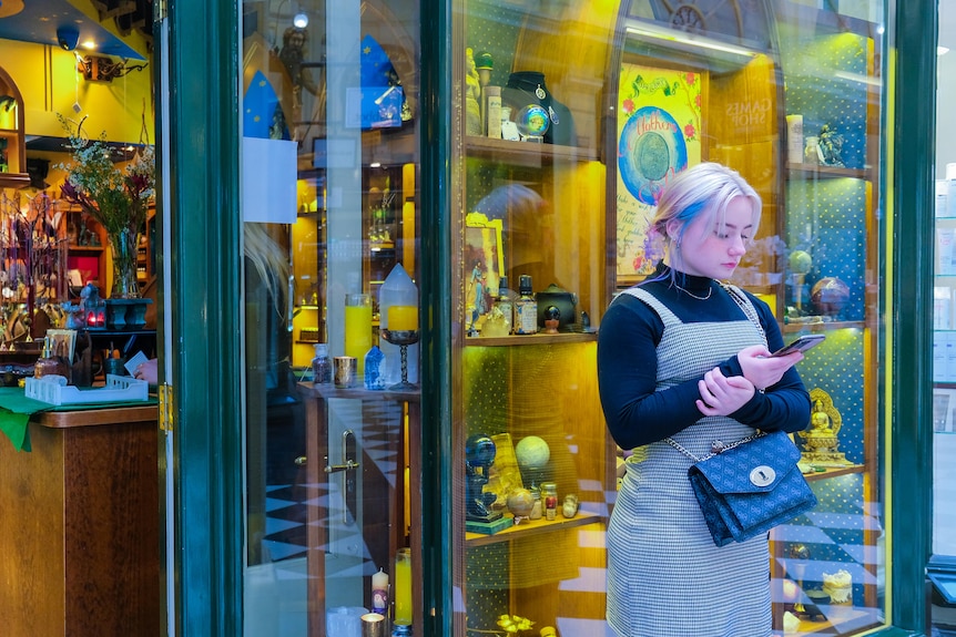 A woman stands outside a Melbourne shop while looking at her phone.