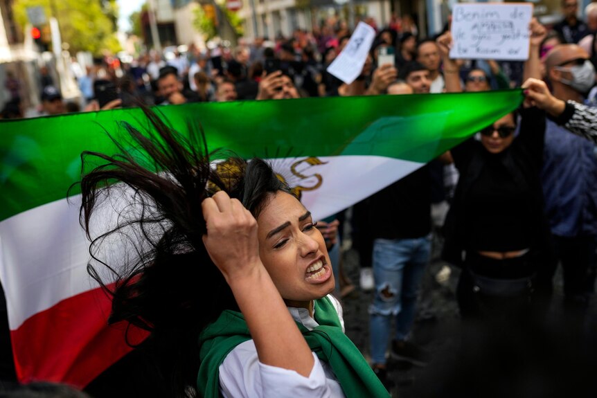 A woman shouts slogans next to an Iranian flag during a protest.