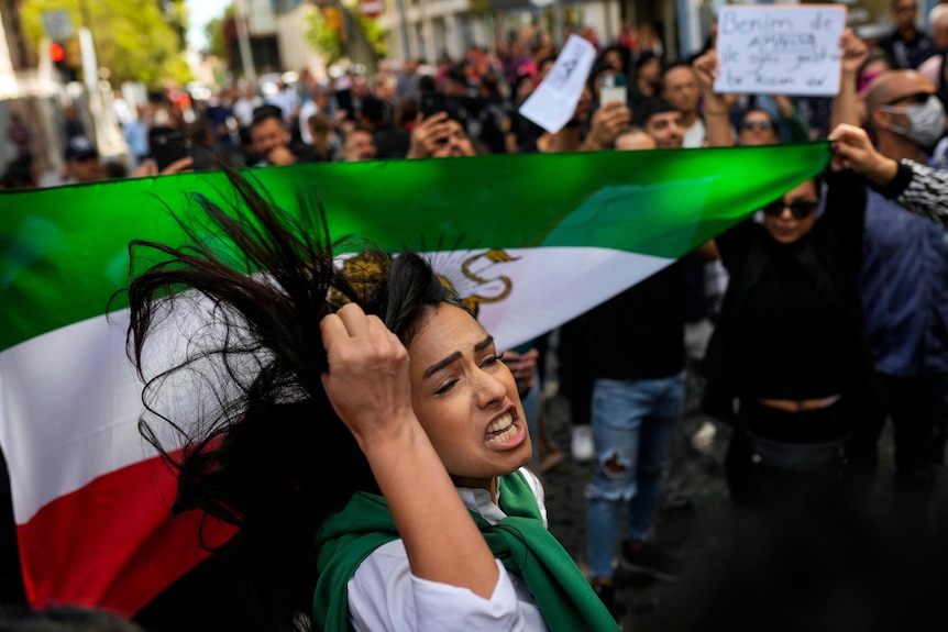 A woman shouts slogans next to an Iranian flag during a protest.