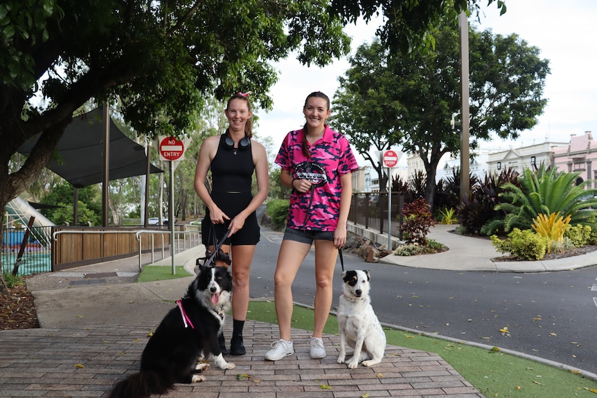 Two woman with exercise gear smile at camera with two dogs