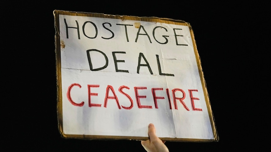 A poster with the words HOSTAGE DEAL CEASEFIRE is held in the air by an obscured hand