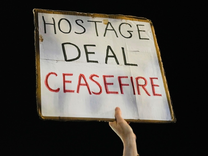 A poster with the words HOSTAGE DEAL CEASEFIRE is held in the air by an obscured hand