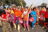 On a Bangladeshi street a large group of women in saris and veils lift their hands and shout in protest.