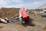 A red and white yacht lies on its side next to a boat trailer.