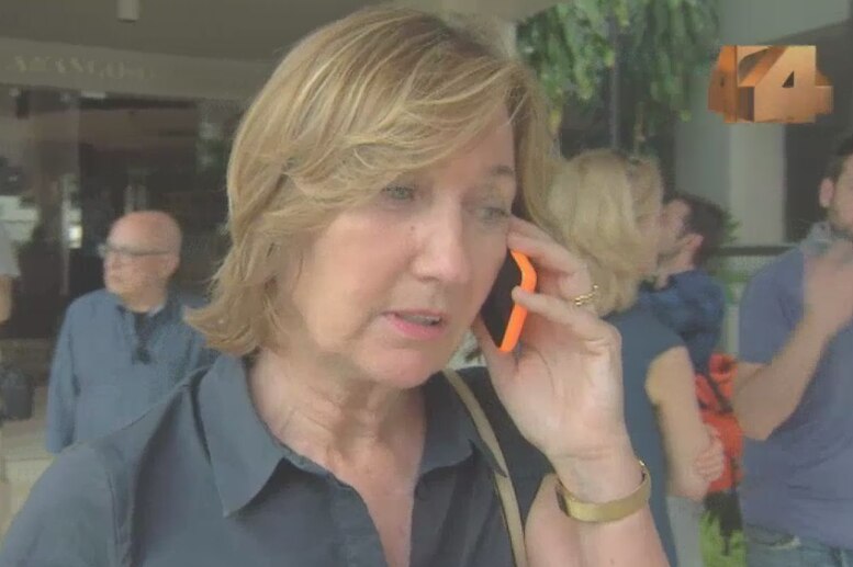Screen shot of Wilkinson on phone with crowd of media behind her.