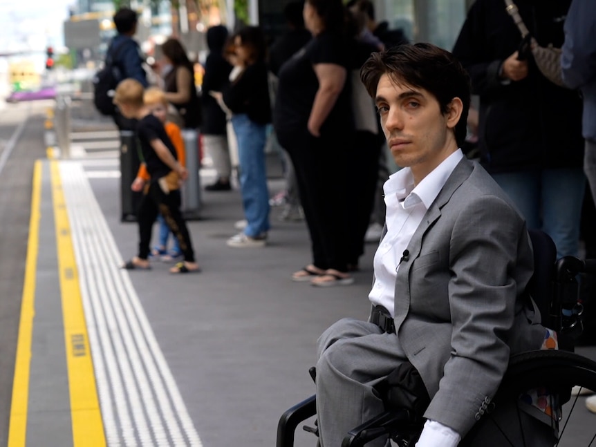 A young man in a wheelchair sits at an accessible tram stop in Melbourne waiting for a tram