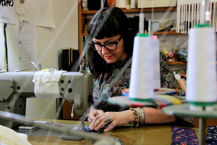 Woman sews a dress at the desk of her dress shop in Braidwood.