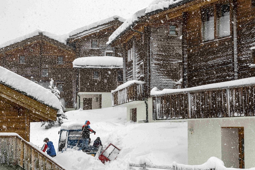 Wooden buildings are covered in snow as snow also falls in front of the camera lens