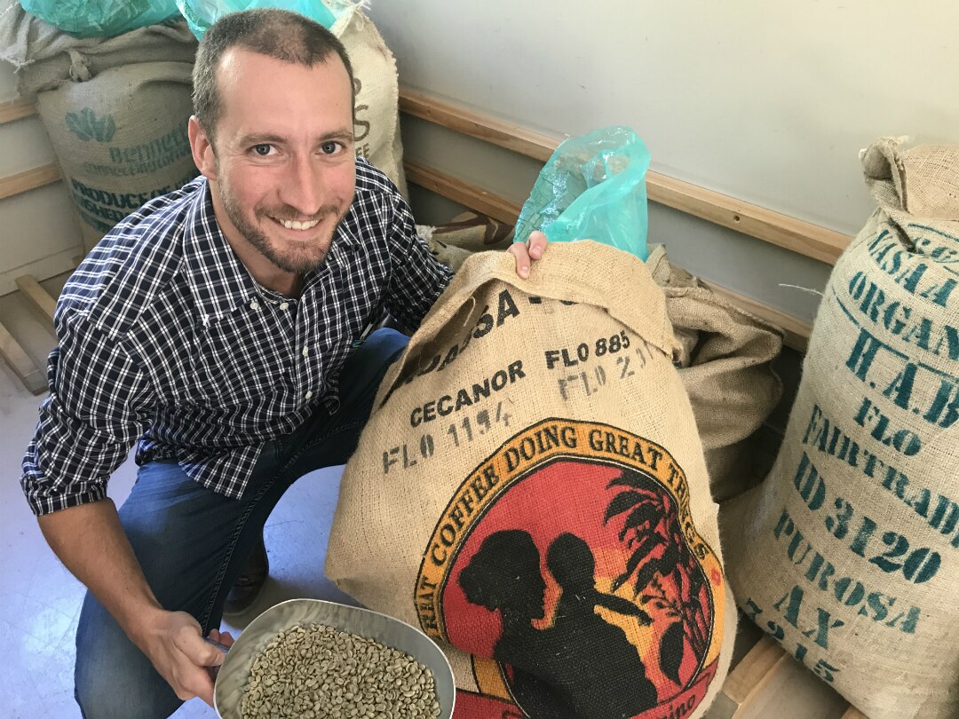 Sean McGowan crouches by bags of coffee beans.