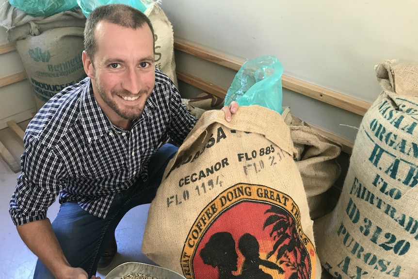 Sean McGowan crouches by bags of coffee beans.