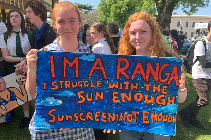 Two red-headed school students hold a sign saying 'I'm a ranga, I struggle with the sun enough.'