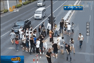 People throw eggs at a naked man tied to a pole in the middle of the road.