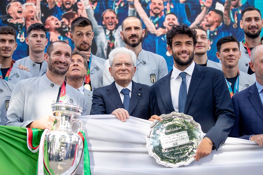 Matteo Berrettini sostiene un trofeo de plata junto al presidente italiano y Giorgio Chiellini