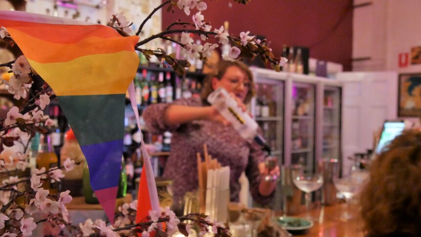 an lgbt+ flag in a bar with a woman pouring drinks behind it