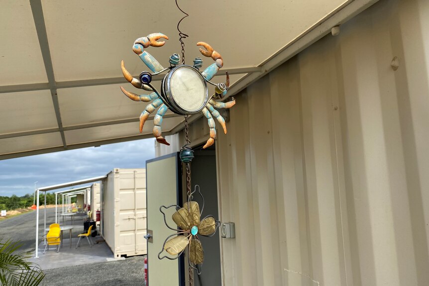 A ceramic and bead decoration hangs from an outdoor awning, shaped like a crab and a flower.