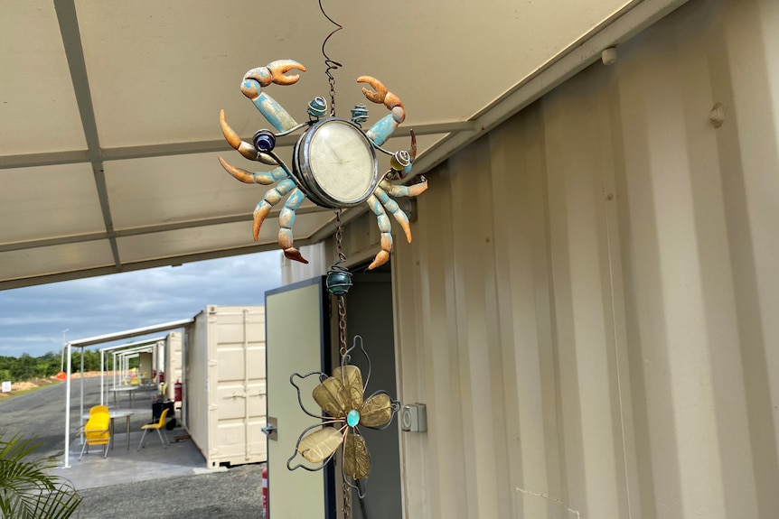 A ceramic and bead decoration hangs from an outdoor awning, shaped like a crab and a flower.