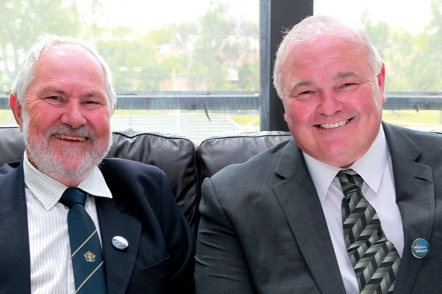 Two men in suits and ties smile at the camera