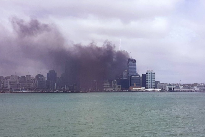A large dark grey smoke cloud billows across the central business district skyline of Auckland