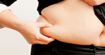 A person's hand squeezing a fat roll on stomach