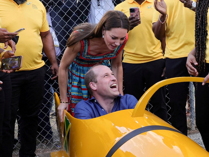 Kate looks down at Prince William who is sitting in a bobsled laughing