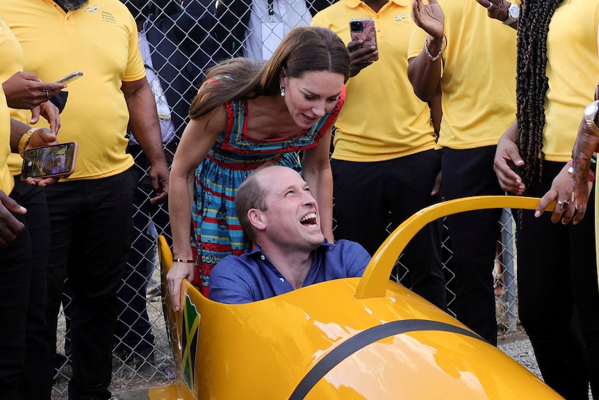 Kate looks down at Prince William who is sitting in a bobsled laughing
