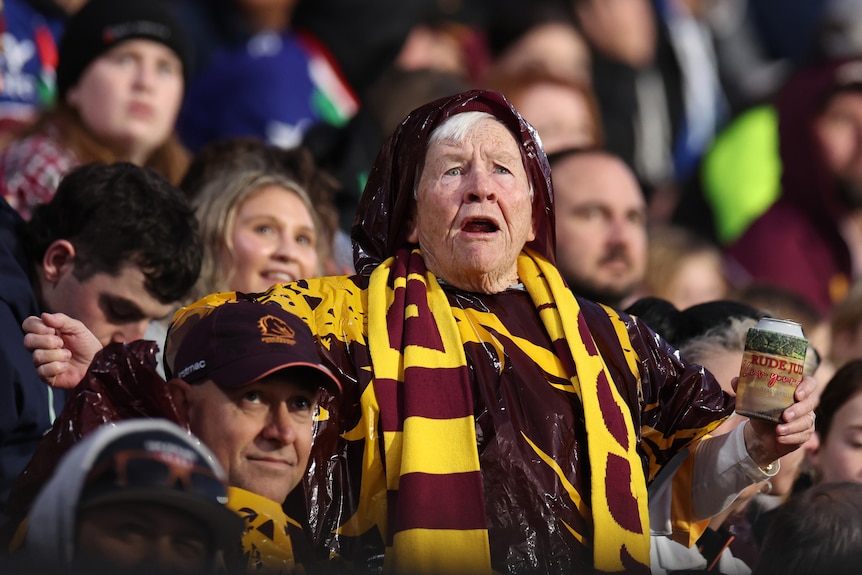 An older Brisbane Broncos fan looks shocked in the stands at an NRL game.