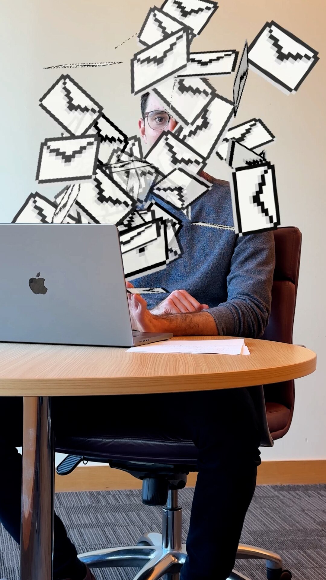 A young man with light-tone skin sits at a table with a laptop open and email icons spilling out covering his face