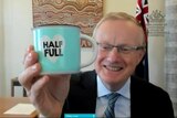 A photo of Reserve Bank Governor Philip Lowe holding a blue mug that says 'half full'