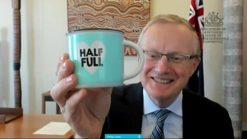 A photo of Reserve Bank Governor Philip Lowe holding a blue mug that says 'half full'