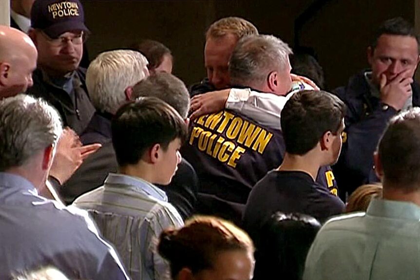 A Newtown police officer is hugged at a vigil for those murdered at the Sandy Hook primary school.