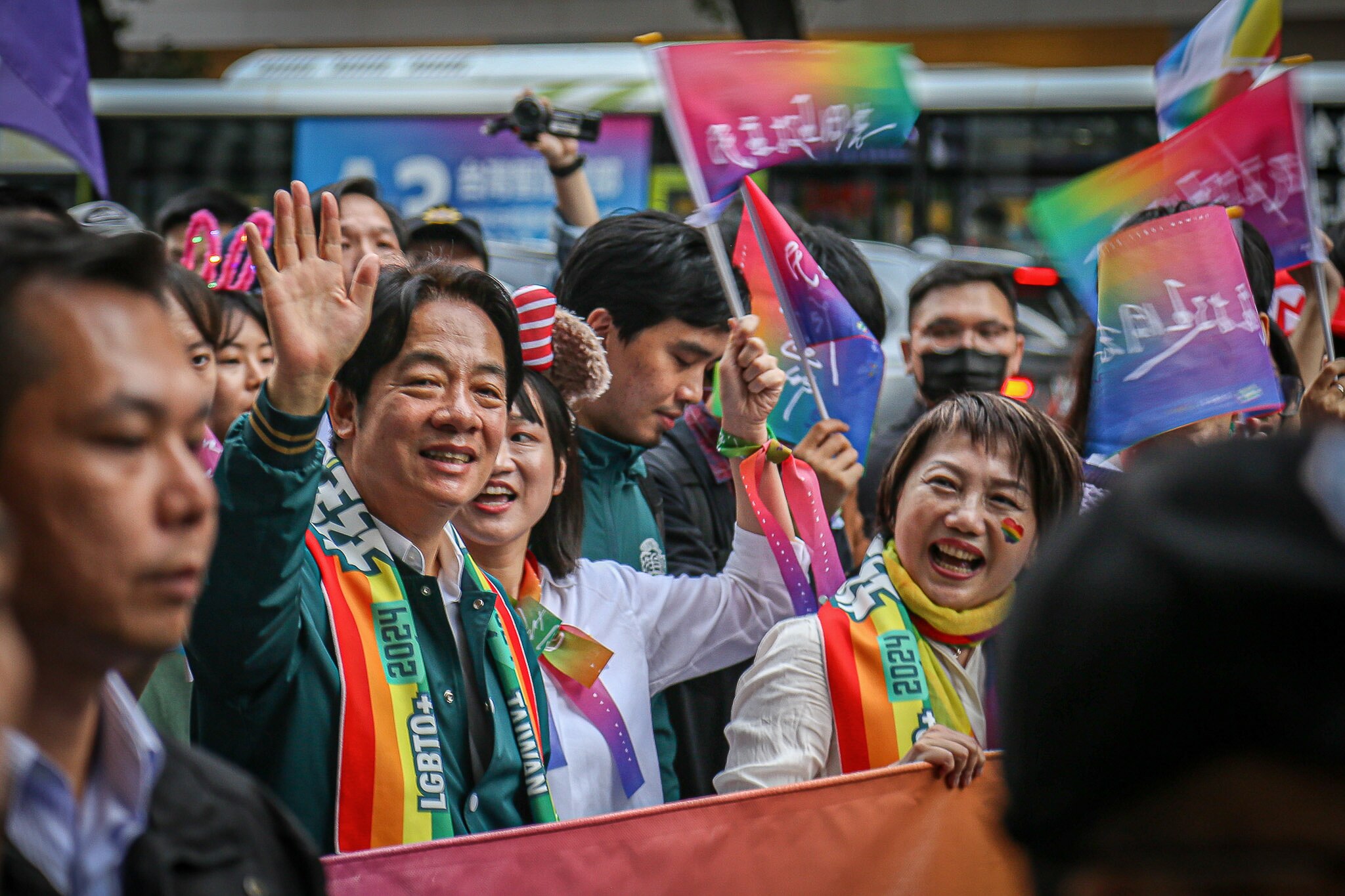 Lai Ching-te smile s and waves in a crowd of people waving rainbow flags