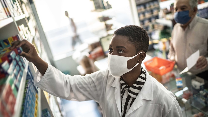 Female pharmacist reaching for medication on high shelf to give to customer.