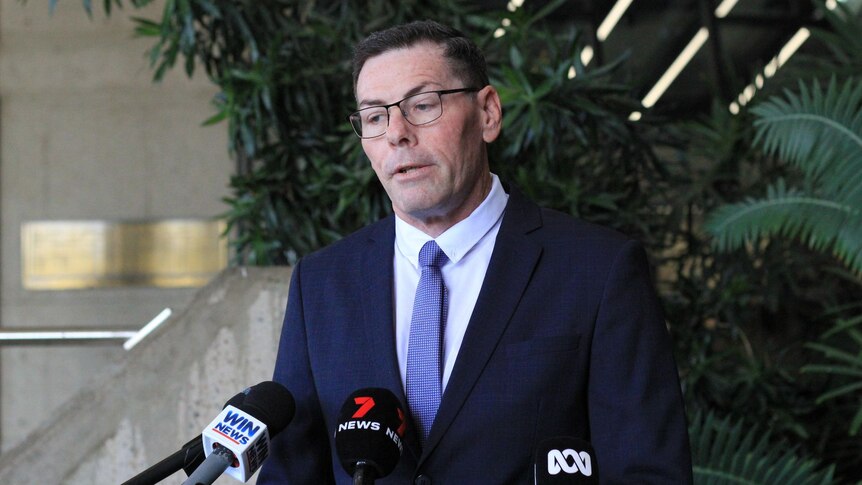 A middle aged man with a black suit speaks before media microphones.