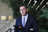 A middle aged man with a black suit speaks before media microphones.