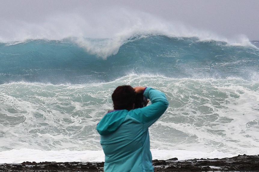 A photographer stands in front of a large wave.