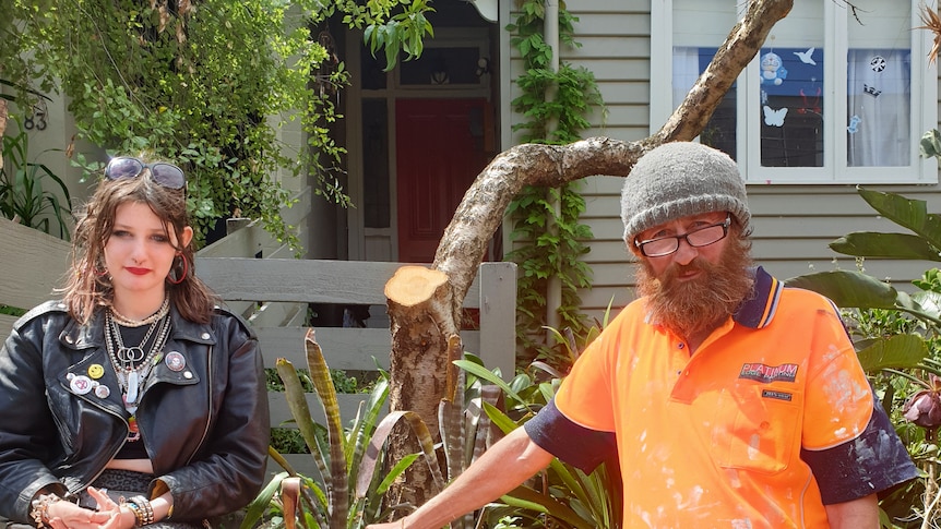 A teen girl and middle aged man sit in front of a tree that has been heavily pruned