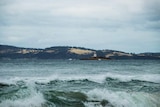 Waves break in a bay with an island in the background