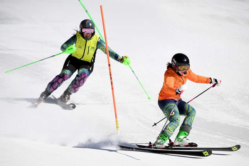 Melissa Perrine wears a yellow hi-vis vest and skis behind her guide, Bobbi Kelly, wearing an orange jacked several metres ahead