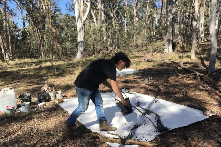 Sophie Cape in bush surrounding using a branch to paint on a large canvas