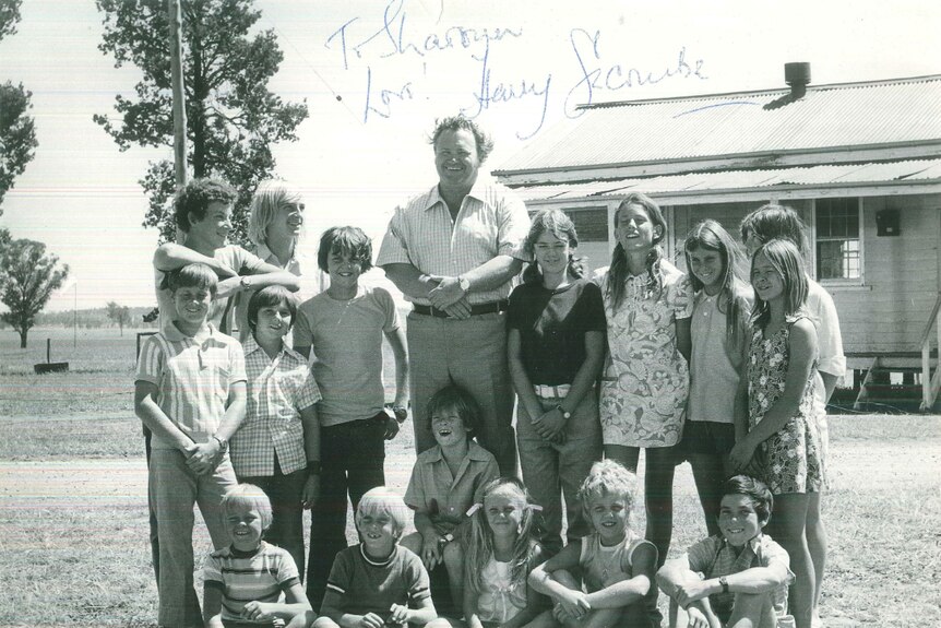 A black and white photo of a group of children standing with an older man, all smiling.