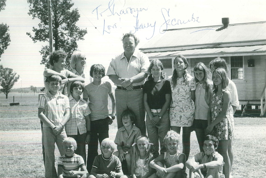 A black and white photo of a group of children standing with an older man, all smiling.