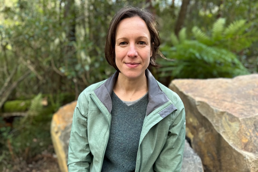 Women with brown hair faces forward with rocks and plant in the background