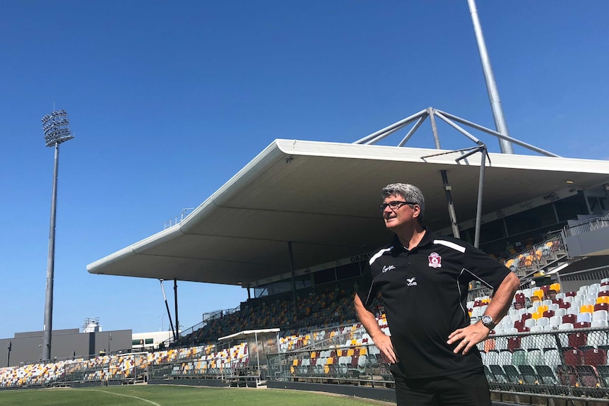 Man standing in a sports stadium, hands on hips, looking into the blue sky